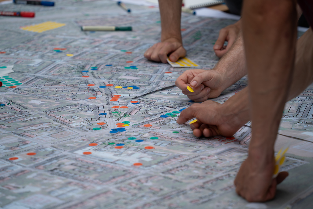 gezeichneter Stadtplan mit bunten Klebepunkten und Händen, die auf dem Plan arbeiten
