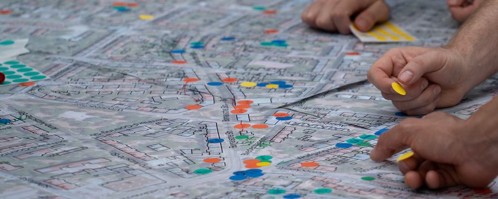 gezeichneter Stadtplan mit bunten Klebepunkten und Händen, die auf dem Plan arbeiten
