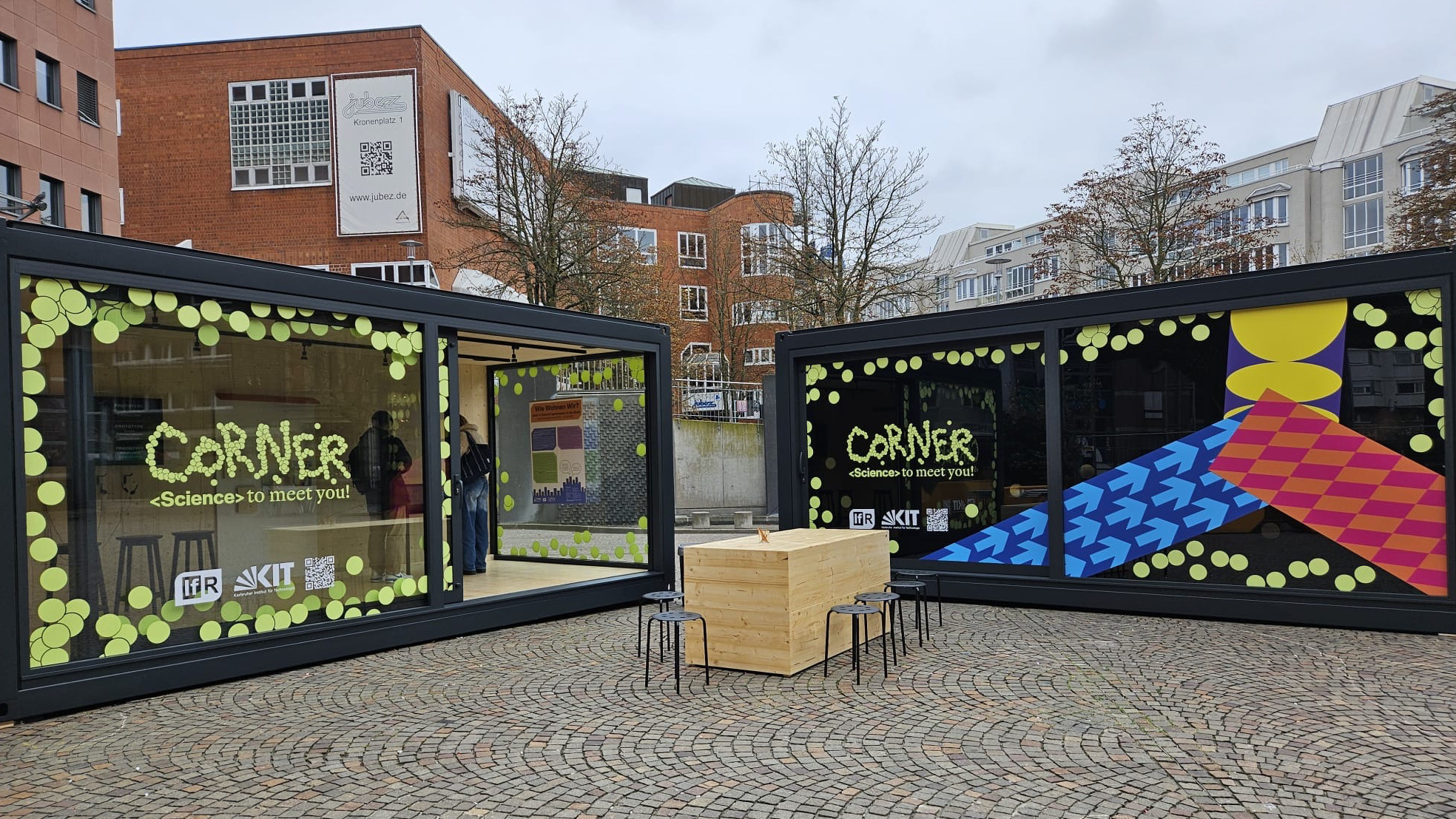 Moderner Wissenschafts-corner mit Sitzgelegenheiten auf urbanem Pflaster vor Gebäuden.